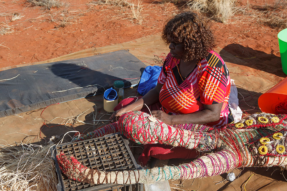 'Paula shapes the sister’s head from wads of <em>tjanpi</em> (grass), stitching them in place with wool.'