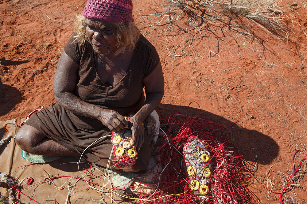 'Angilyiya makes small raffia donut-shapes to create the <em>walka</em> (body design) used for <em>inma</em> (ceremonial song and dance) at the Kuru Ala site, where dancing and singing of the Seven Sisters Tjukurrpa (Dreaming) takes place.'