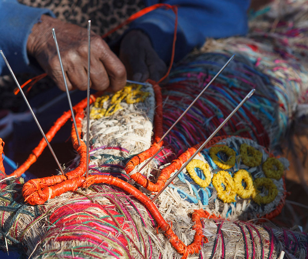 'Janet uses large sailmaker needles to hold the <em>walka</em> (body decoration) while she sews it into place. These detailed and colourful designs are specific to the Kuru Ala <em>inma</em> (ceremonial song and dance).'